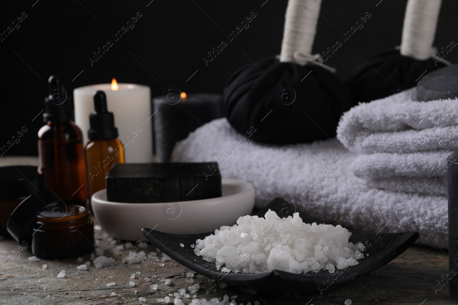 Photo of Spa composition. Sea salt, soap bar and towels on grey textured table, closeup