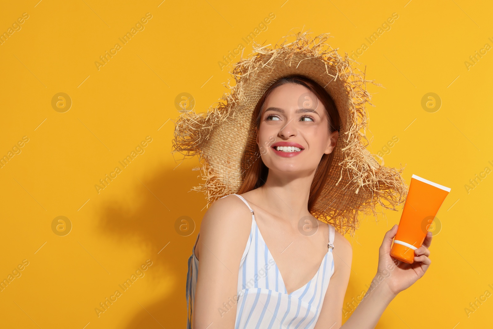 Photo of Beautiful young woman in straw hat holding sun protection cream on orange background, space for text