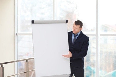 Photo of Business trainer giving presentation on flip chart board indoors