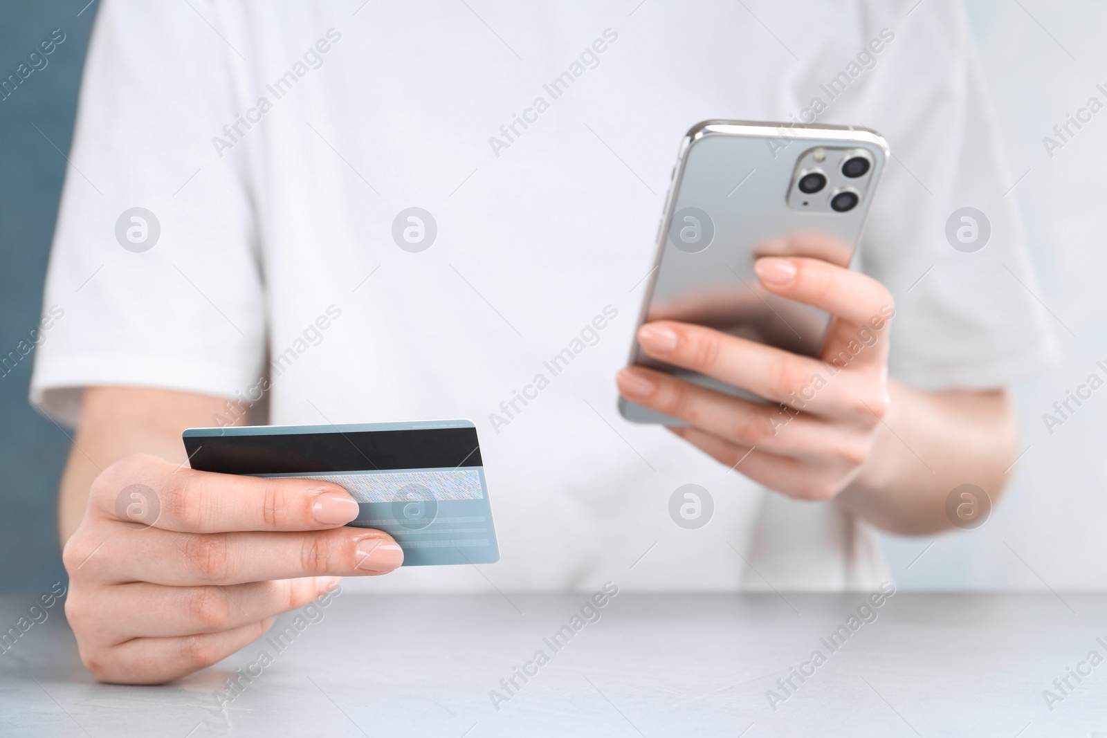 Photo of Online payment. Woman with smartphone and credit card at white table, closeup