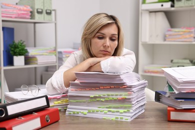 Photo of Overwhelmed woman surrounded by documents at workplace in office