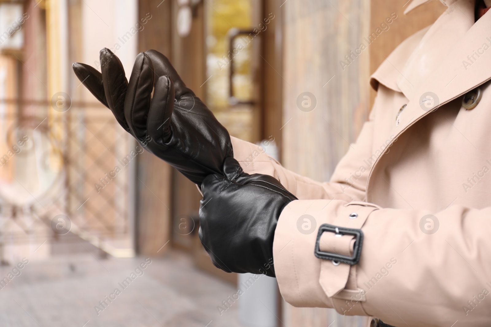 Photo of Stylish man putting on black leather gloves outdoors, closeup