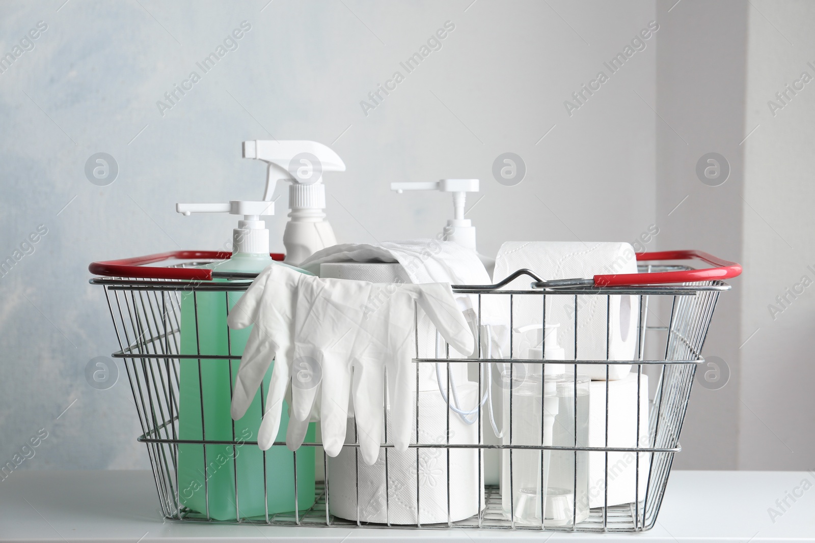 Photo of Shopping basket with antiseptics, toilet paper, gloves  and masks on table indoors. Panic caused by virus
