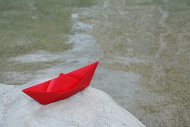 Beautiful red paper boat on stone outdoors. Space for text