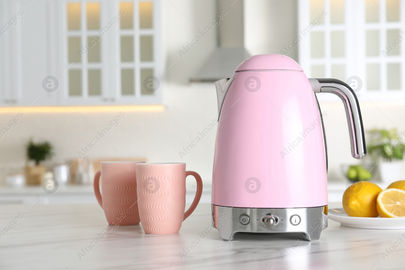 Photo of Modern electric kettle, cups and lemons on table in kitchen