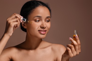 Beautiful woman applying serum onto her face on brown background