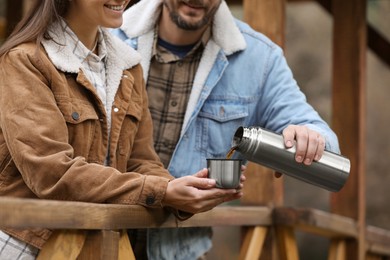 Boyfriend pouring hot drink from metallic thermos into cup lid for his girlfriend outdoors, closeup