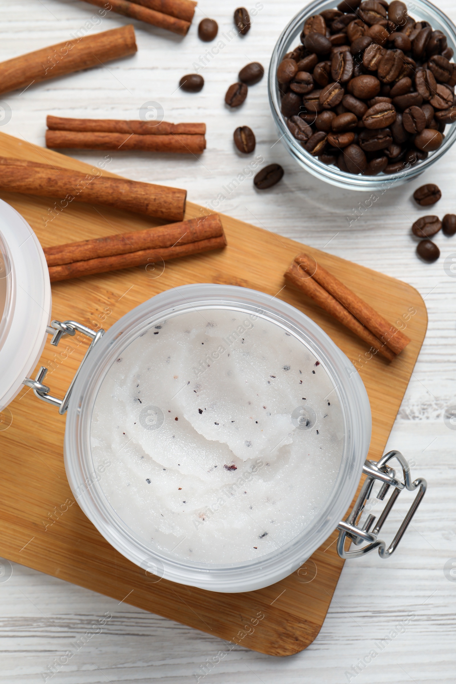 Photo of Body scrub in glass jar, cinnamon and coffee beans on white wooden table, flat lay