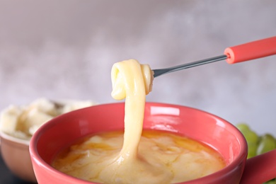 Dipping bread into pot with cheese fondue, closeup