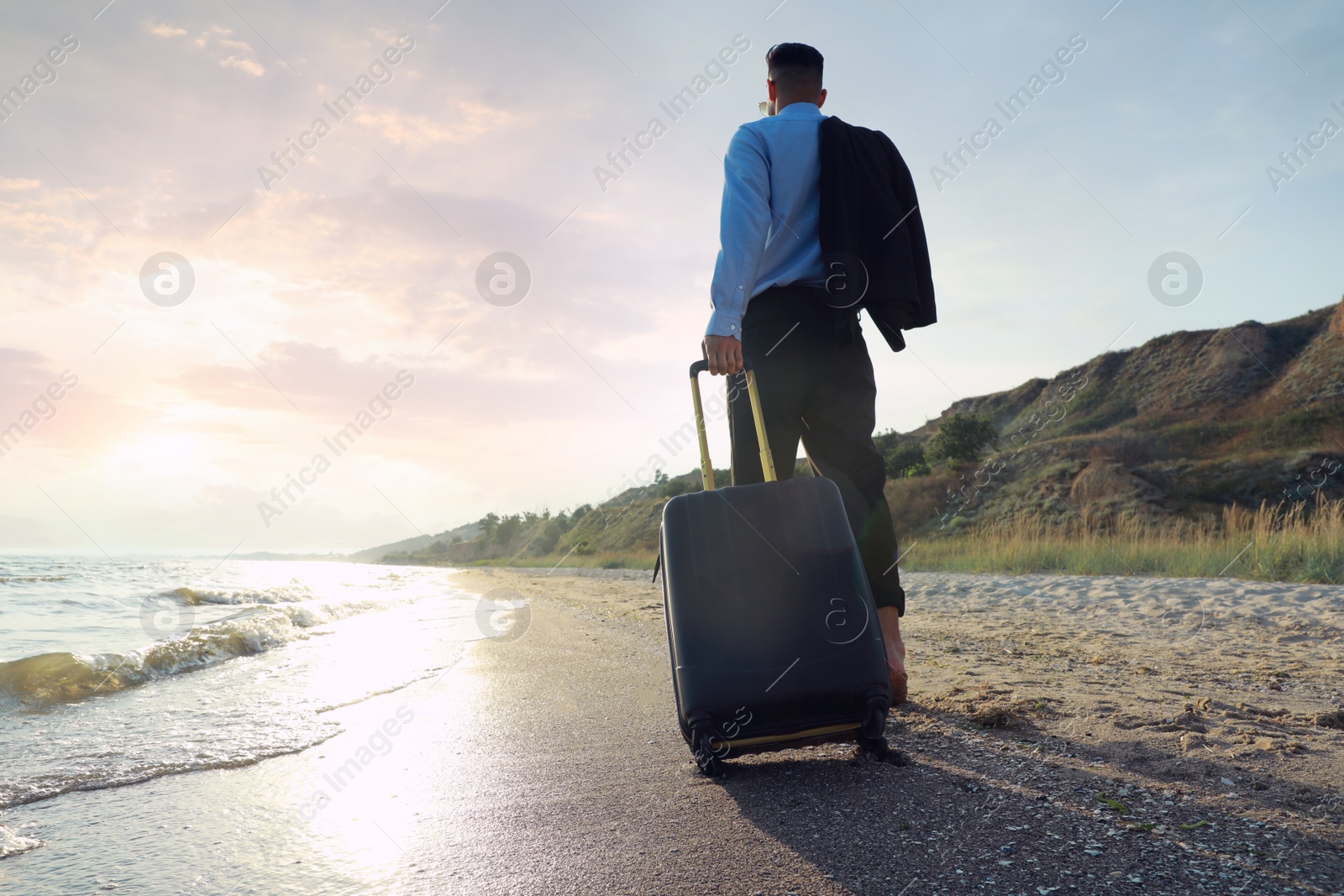 Photo of Businessman with suitcase walking on beach, low angle view. Business trip