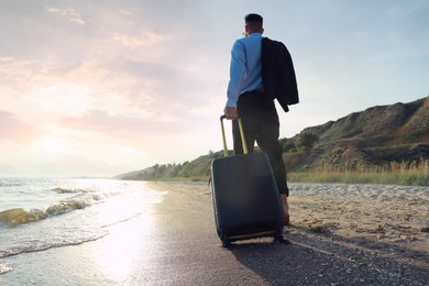 Photo of Businessman with suitcase walking on beach, low angle view. Business trip