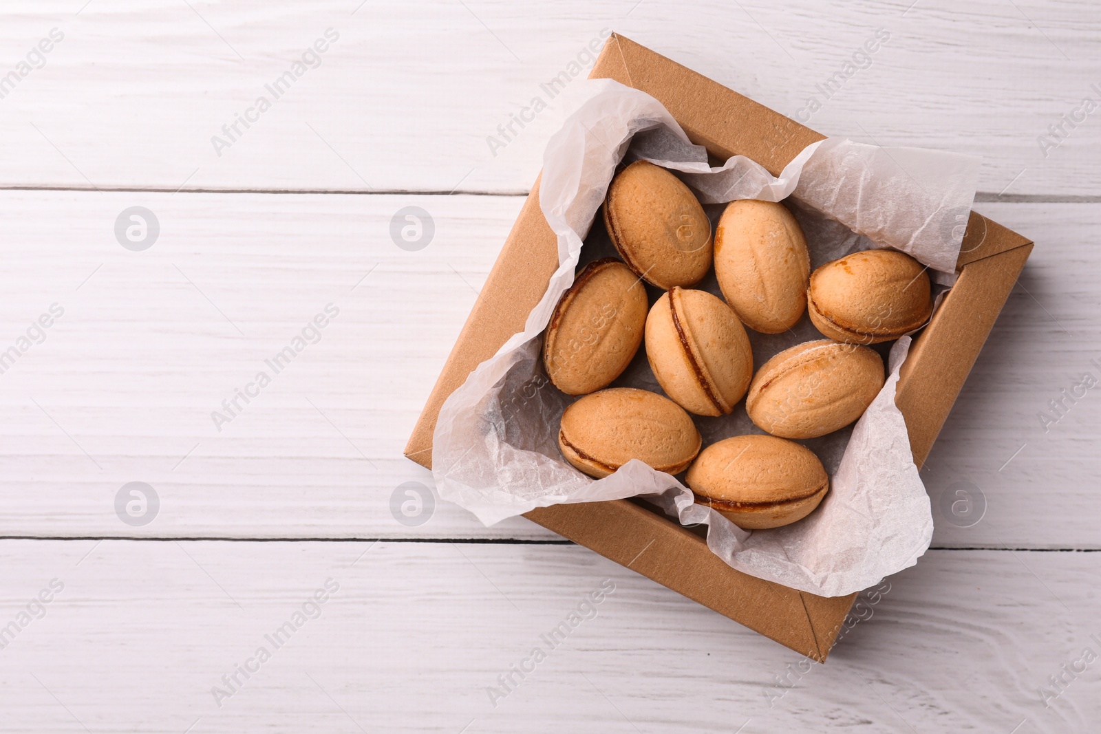 Photo of Delicious nut shaped cookies with boiled condensed milk in box on white wooden table, top view