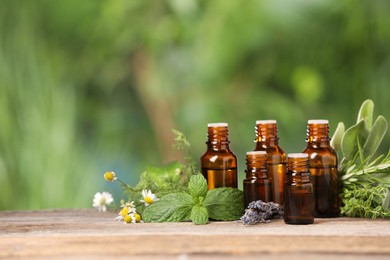 Photo of Bottles with essential oils and plants on wooden table against blurred green background. Space for text