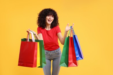 Photo of Happy young woman with shopping bags on yellow background