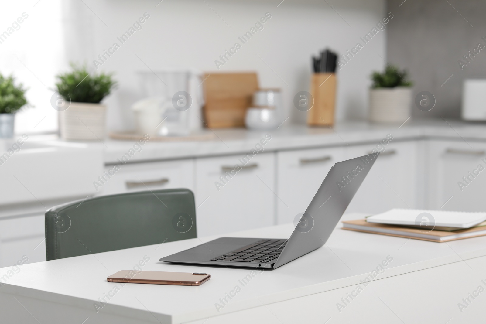 Photo of Home office. Laptop, smartphone and stationery on white desk in kitchen, space for text