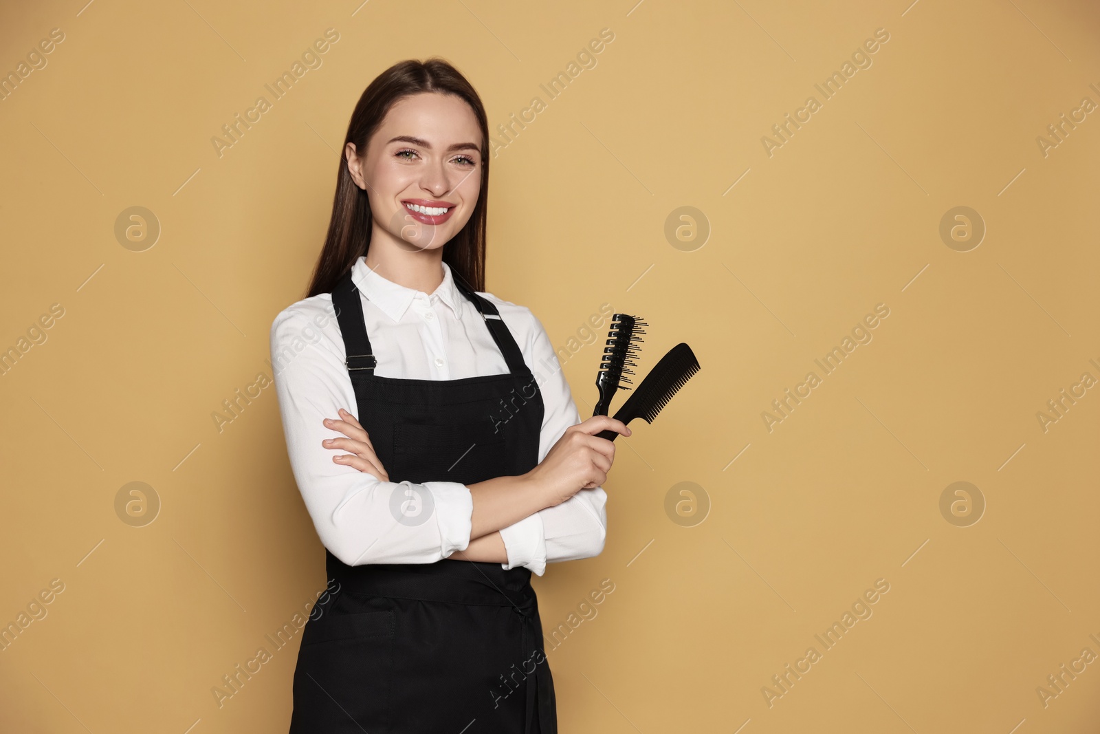 Photo of Portrait of happy hairdresser with brush and comb on beige background. Space for text