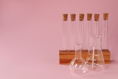 Photo of Flasks and test tubes on pink background, space for text. Laboratory glassware