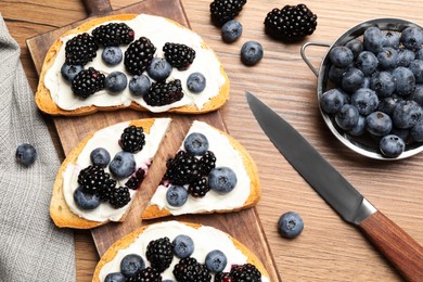 Photo of Tasty sandwiches with cream cheese, blueberries and blackberries on wooden table, flat lay