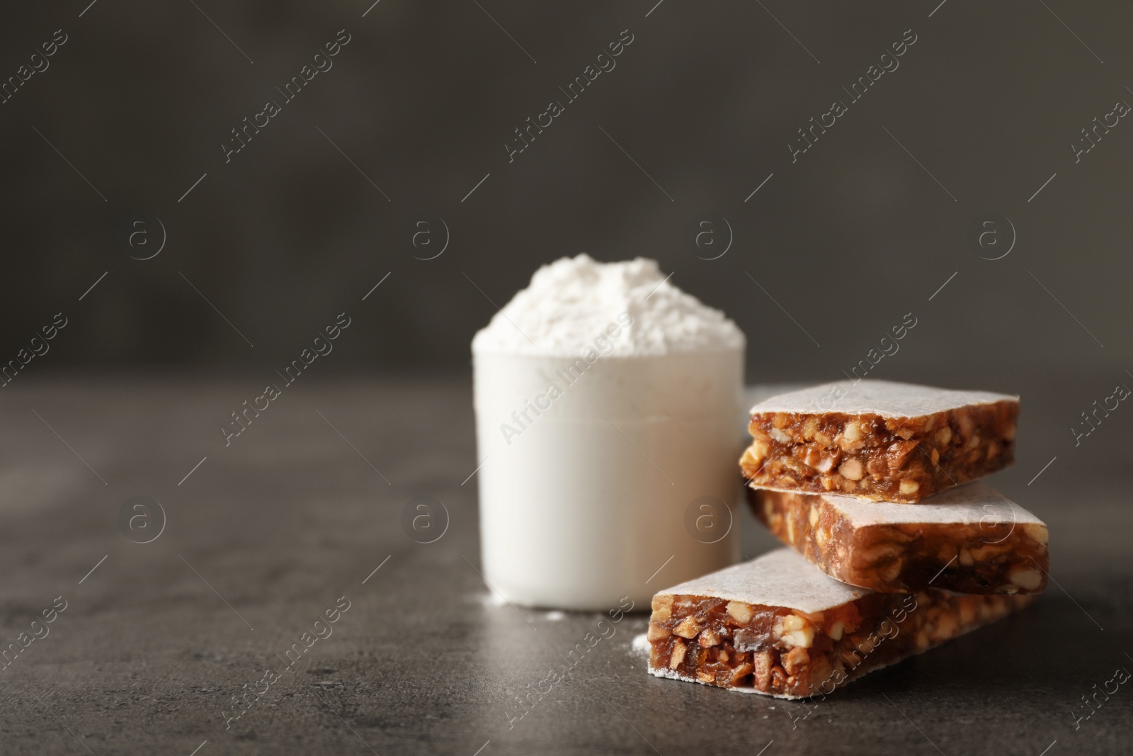 Photo of Tasty protein bars and scoop of powder on grey table. Space for text