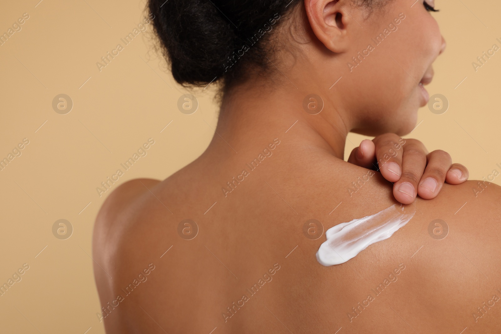 Photo of Young woman applying body cream onto back on beige background, closeup