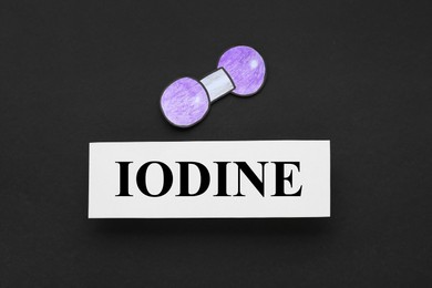 Photo of Card with word Iodine and atom shape made of paper on black background, flat lay