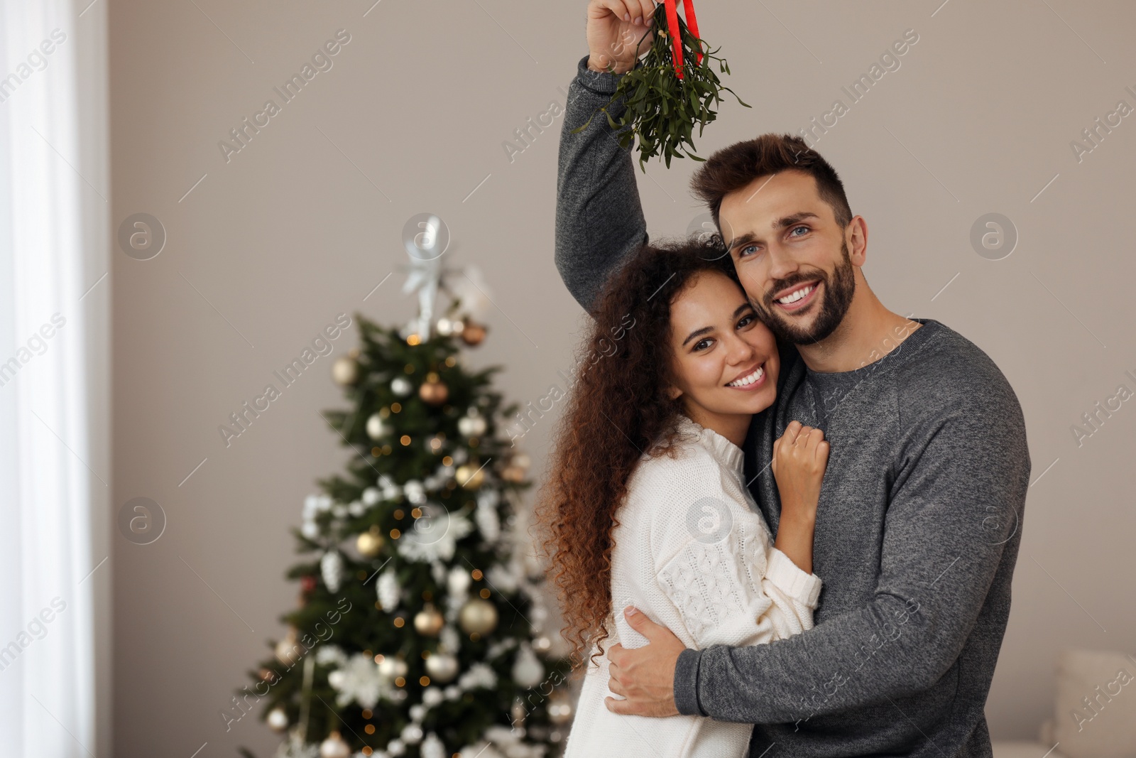 Photo of Portrait of lovely couple under mistletoe bunch in room decorated for Christmas