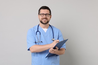 Photo of Smiling doctor with clipboard on light grey background