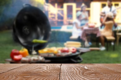 Empty black wooden table and blurred view of tasty food on modern barbecue grill outdoors