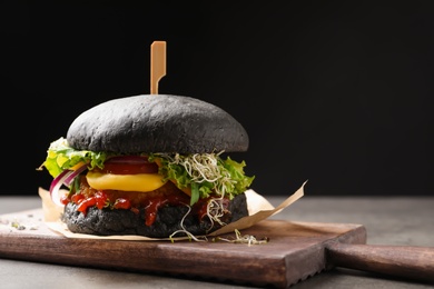 Photo of Board with tasty black vegetarian burger on table against dark background