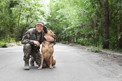 Photo of Man in military uniform with German shepherd dog, outdoors