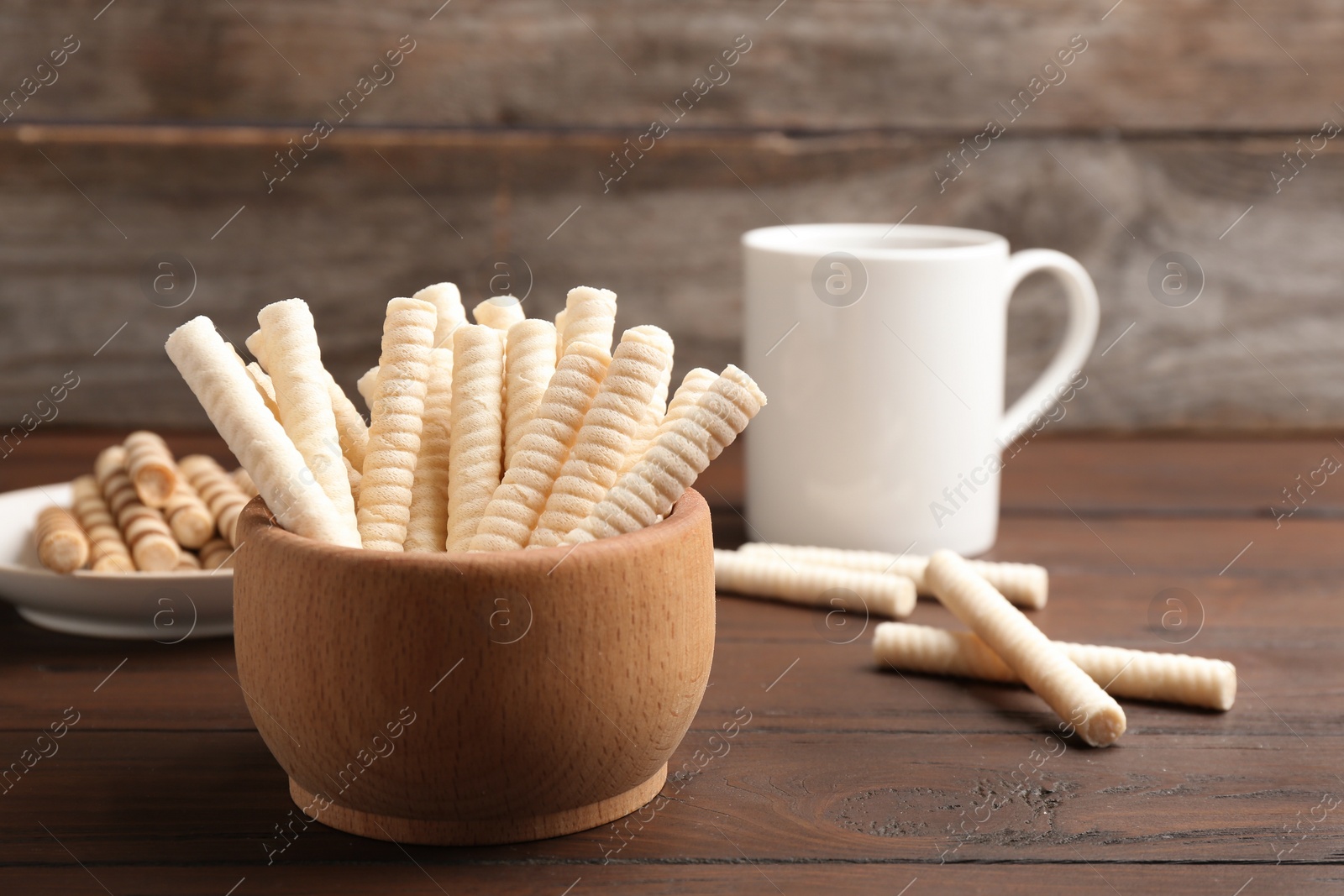 Photo of Bowl with wafer rolls on wooden table, space for text