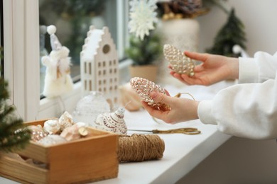 Woman holding Christmas baubles in shape of cones near window sill indoors, closeup