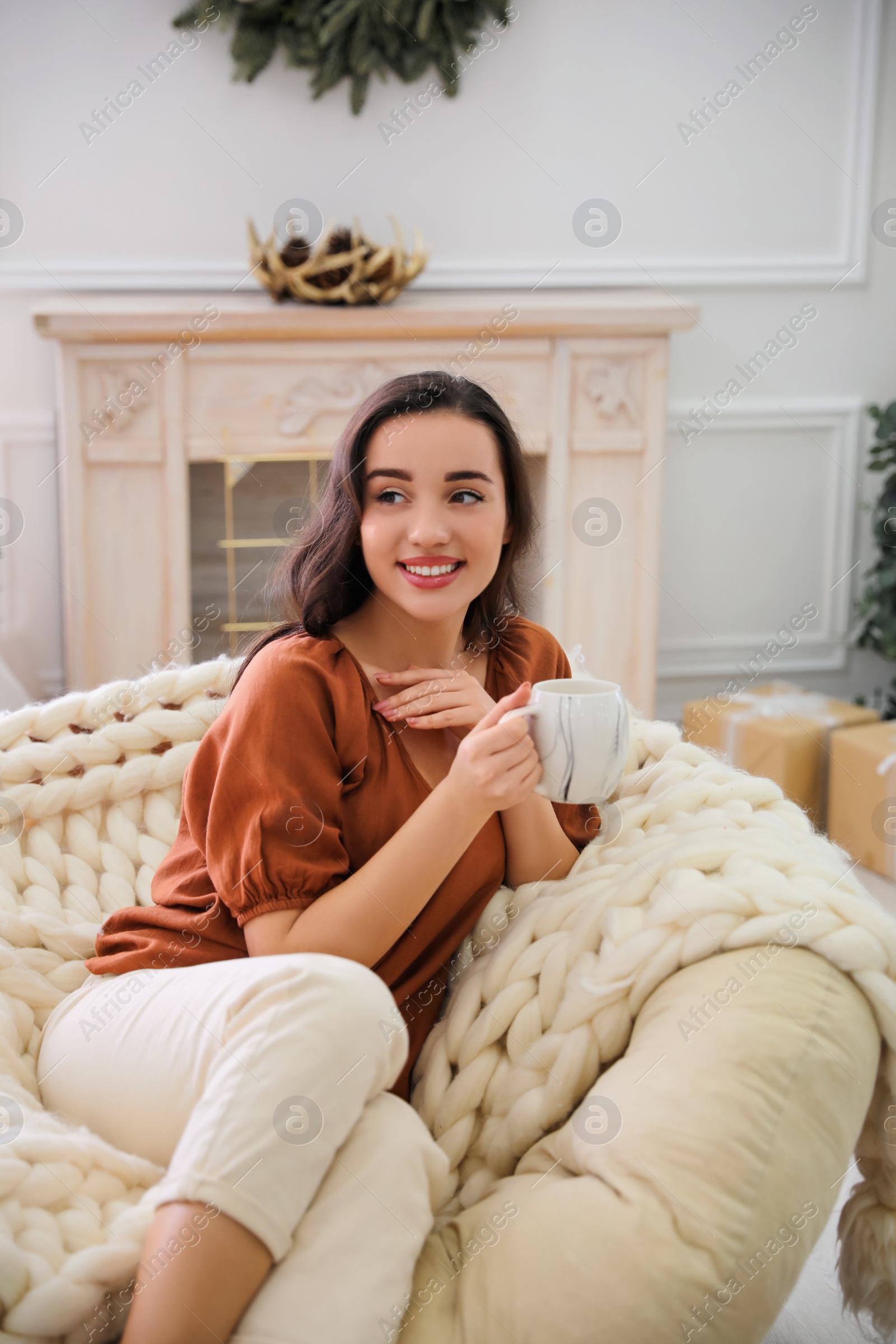 Photo of Woman with hot drink resting in comfortable papasan chair at home