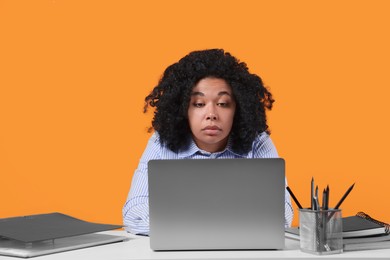Photo of Stressful deadline. Tired woman looking at laptop at white table on orange background