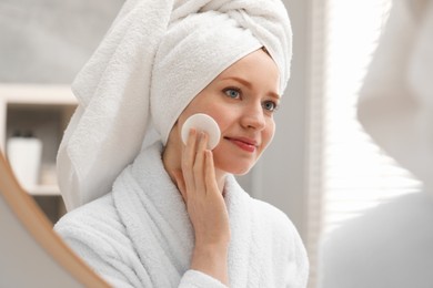 Beautiful woman with freckles wiping face near mirror in bathroom