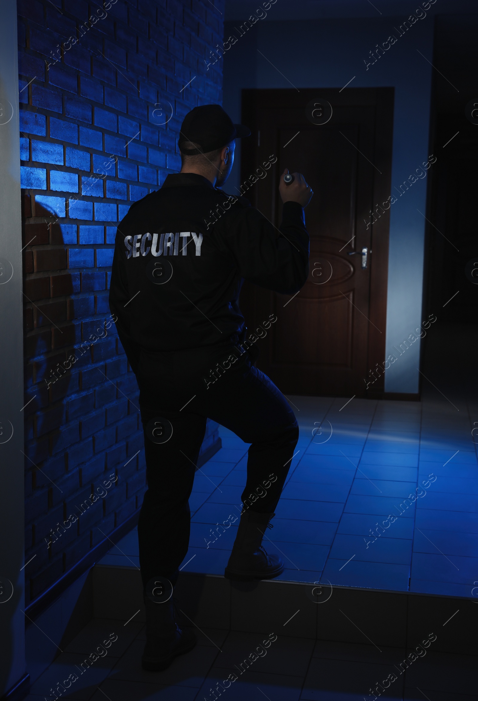 Photo of Male security guard with flashlight in dark corridor