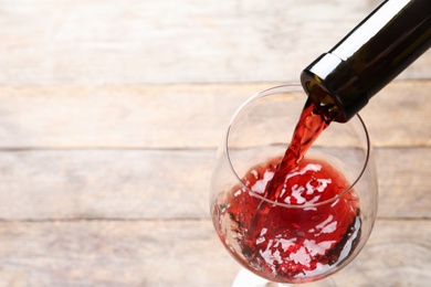 Pouring red wine from bottle into glass on blurred background, closeup. Space for text