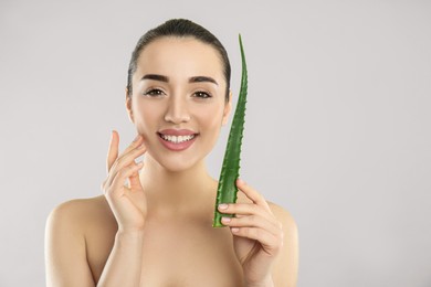 Photo of Young woman with aloe vera leaf on light grey background. Space for text