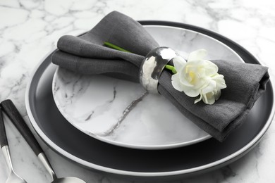 Stylish setting with cutlery, napkin, flowers and plates on white marble table, closeup