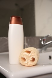 Photo of Natural loofah sponge and bottle of shower gel on washbasin in bathroom