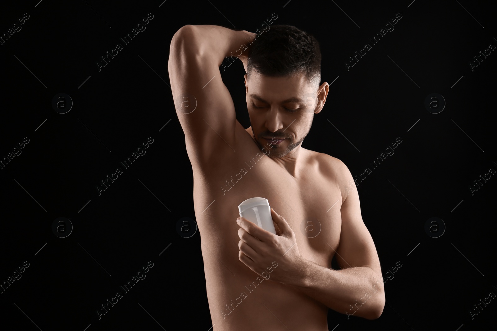 Photo of Handsome man applying deodorant on black background