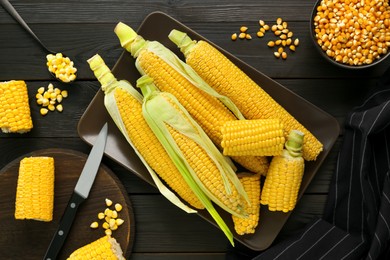 Photo of Tasty fresh corn cobs and kernels on black wooden table, flat lay
