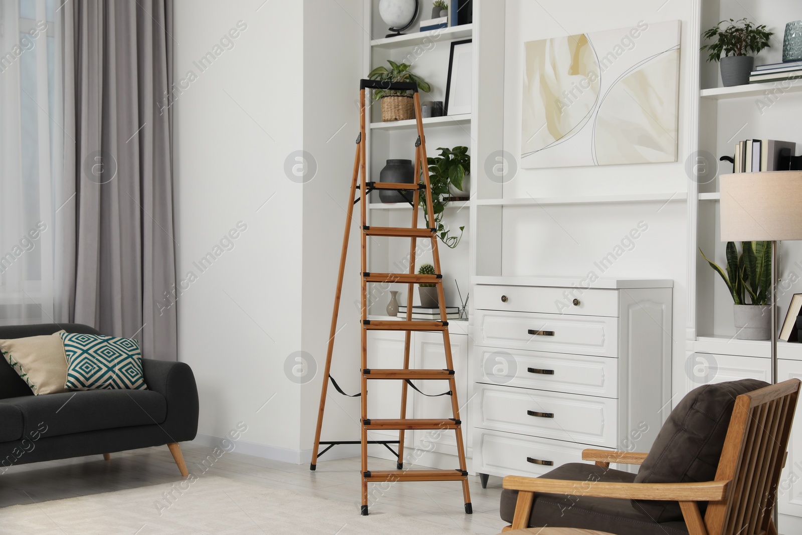 Photo of Wooden folding ladder near chest of drawers and shelves with accessories in room