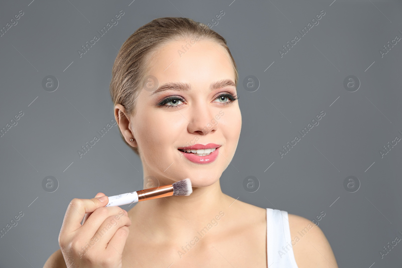 Photo of Beautiful woman applying makeup with brush on light grey background