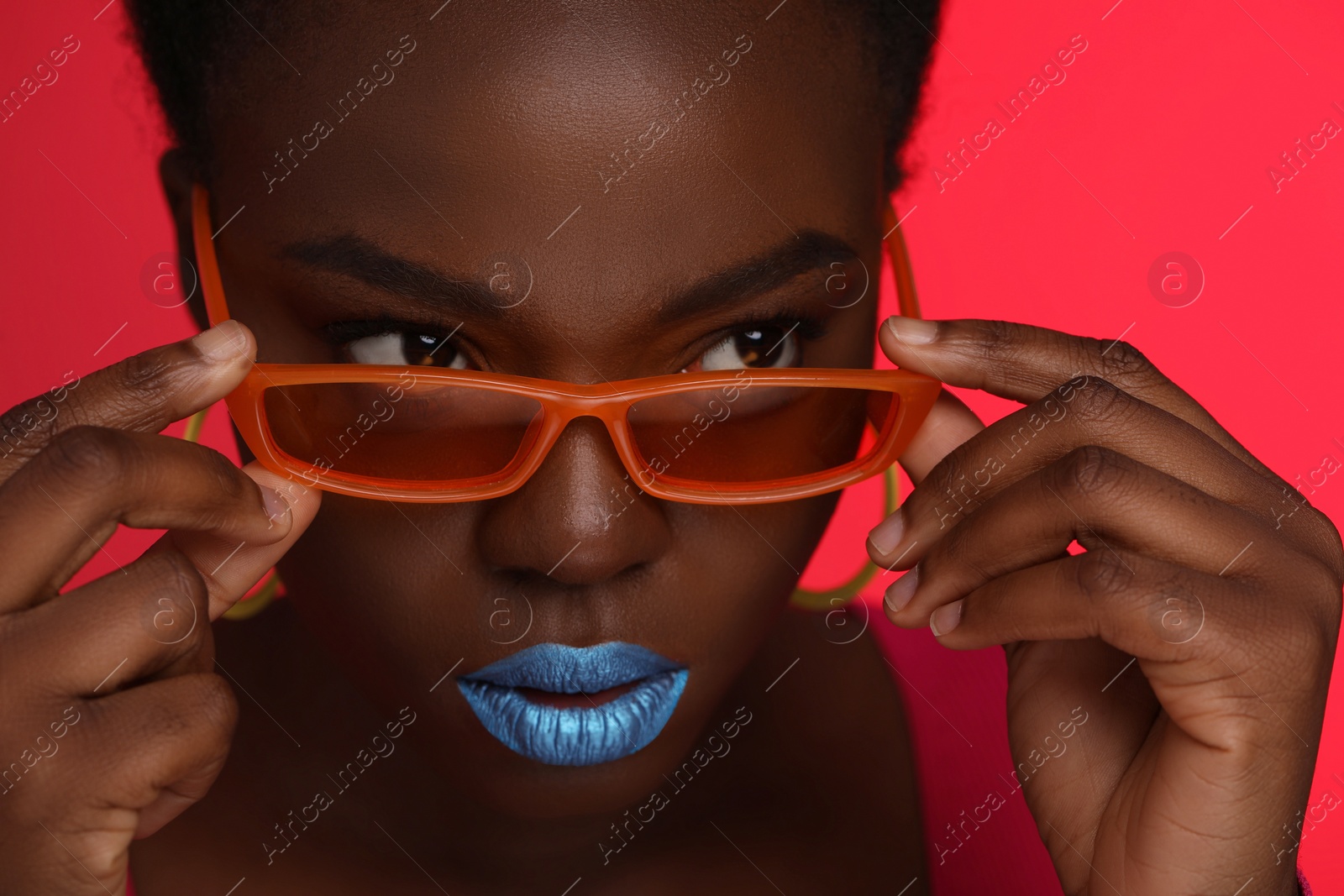 Photo of Fashionable portrait of beautiful woman with stylish sunglasses on coral background, closeup