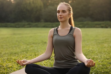 Beautiful woman practicing yoga in park. Lotus pose