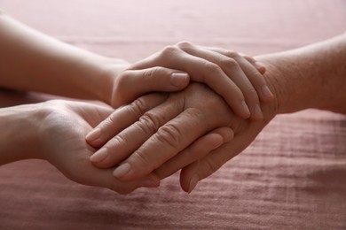 Photo of Young and elderly women holding hands together on pink fabric, closeup