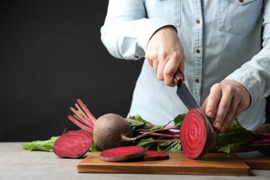 Woman cutting fresh red beet at table, closeup