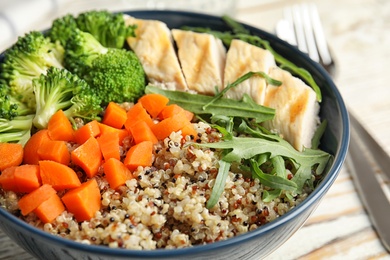 Photo of Ceramic bowl with quinoa and garnish on table, closeup