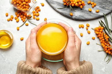 Photo of Woman holding cup with sea buckthorn tea at grey table, top view